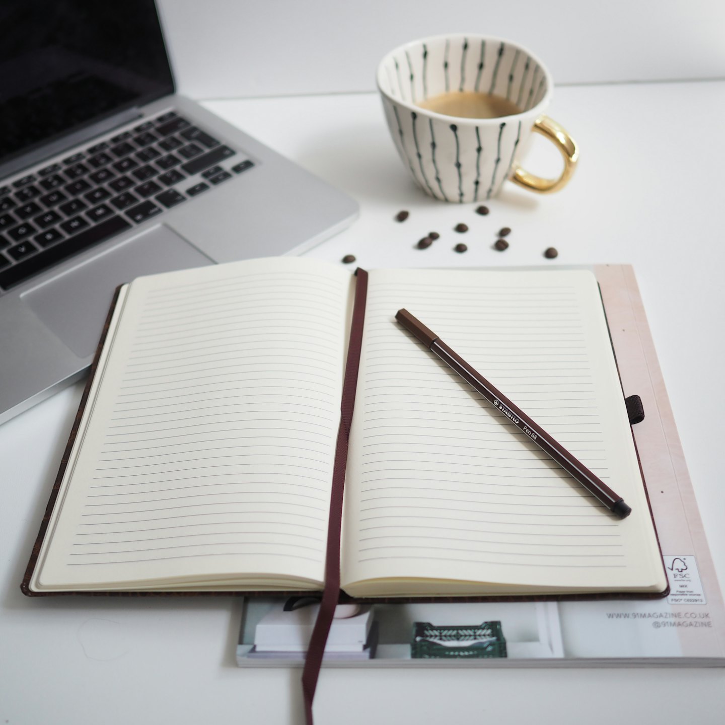 Bovenaanzicht van een minimalistisch bureau met laptop, notitieboekje en koffiekopje.