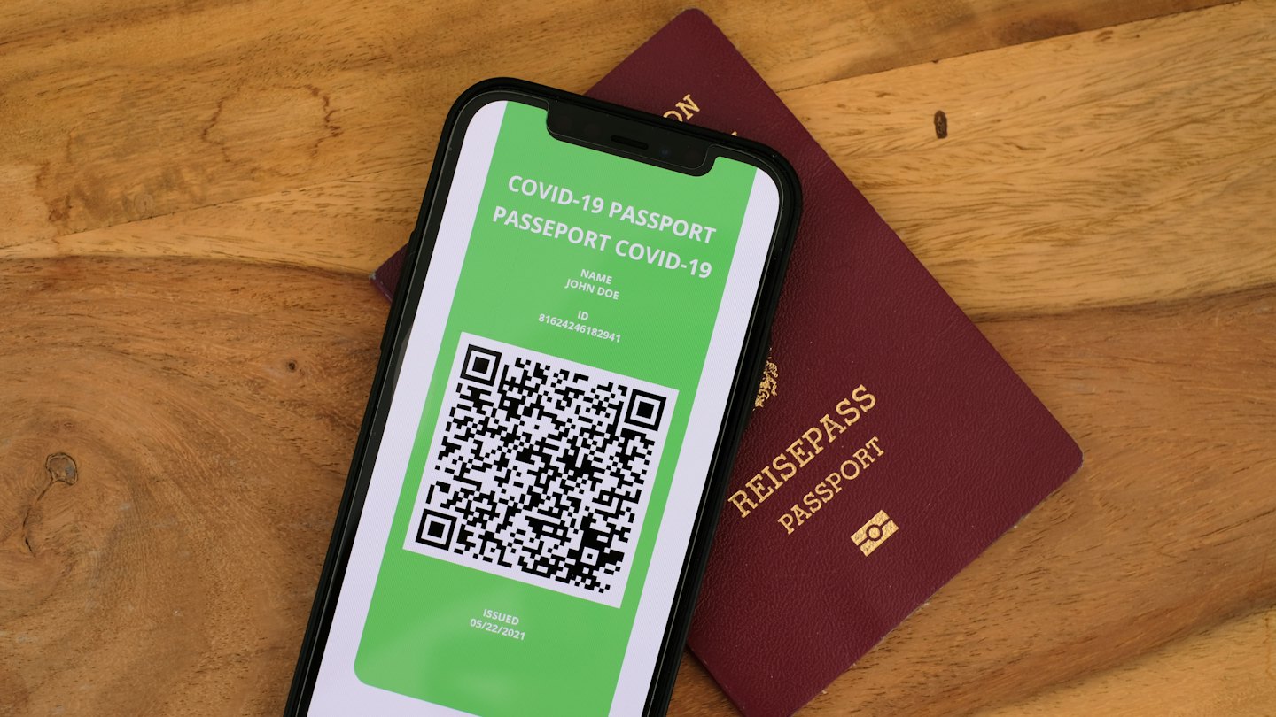 Smartphone met COVID-19-paspoort ligt op fysiek paspoort.