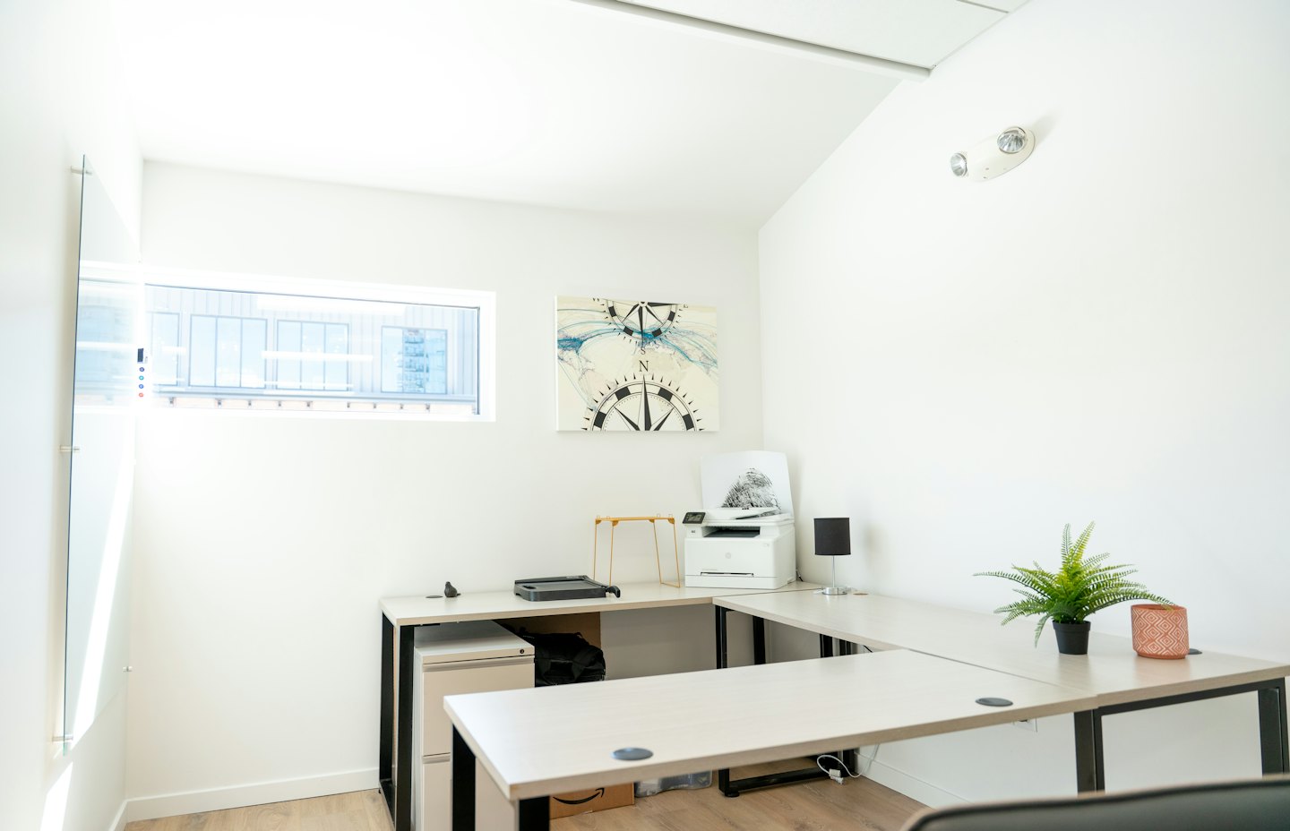 Minimalistisch thuiskantoor met een L-vormig bureau en een kompas-kunstwerk.