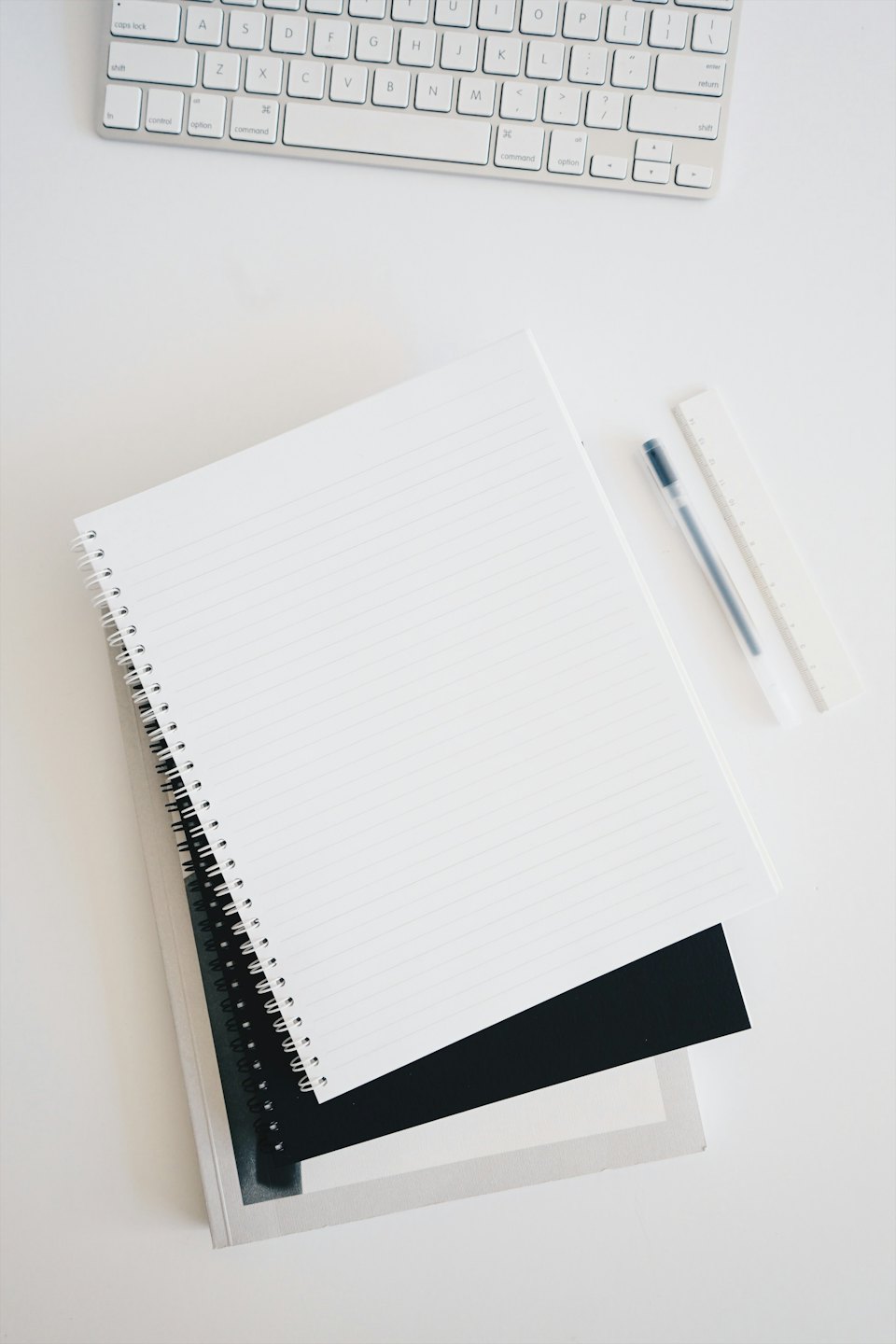 Minimalistische werkplek met notitieboekjes, pen, liniaal en toetsenbord.